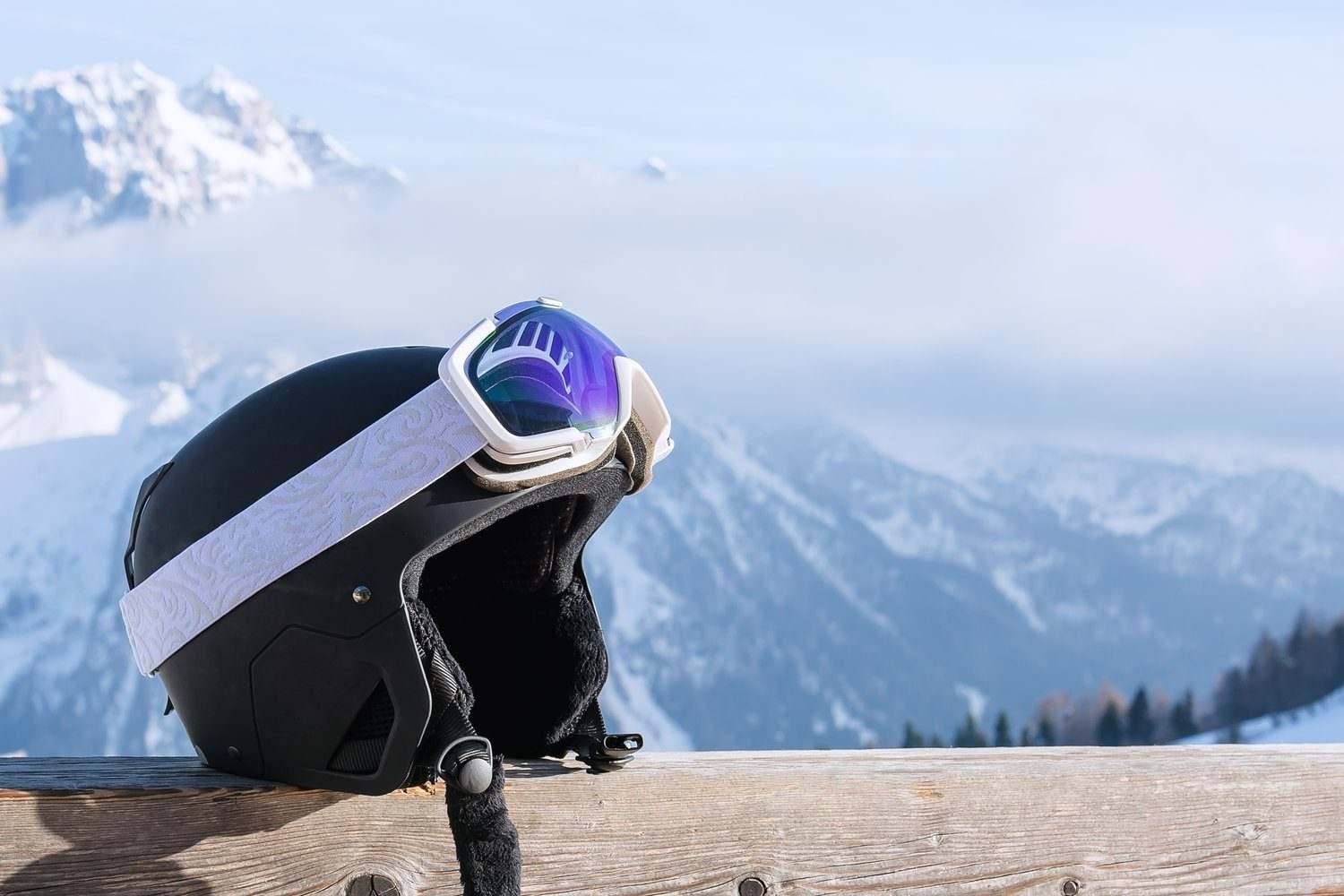 Kask i gogle narciarskie na drewnianej barierce, w tle ośnieżone góry